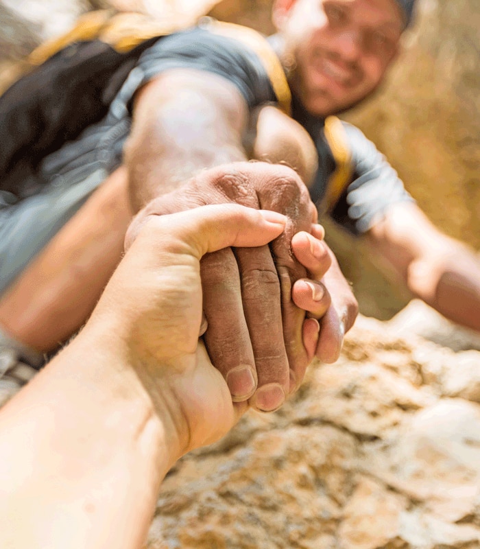 A manextending a hand to a fellow rock climber